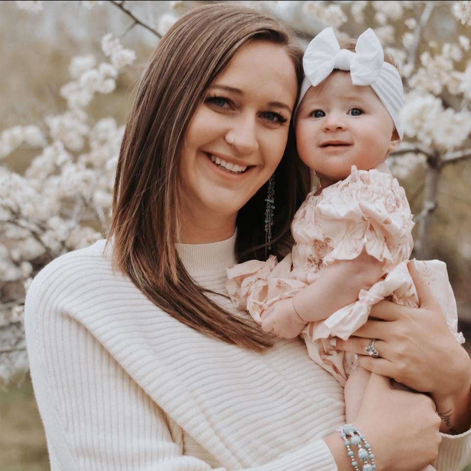 Kaitlyn smiling with a baby in her arms beneath white spring blossoms.