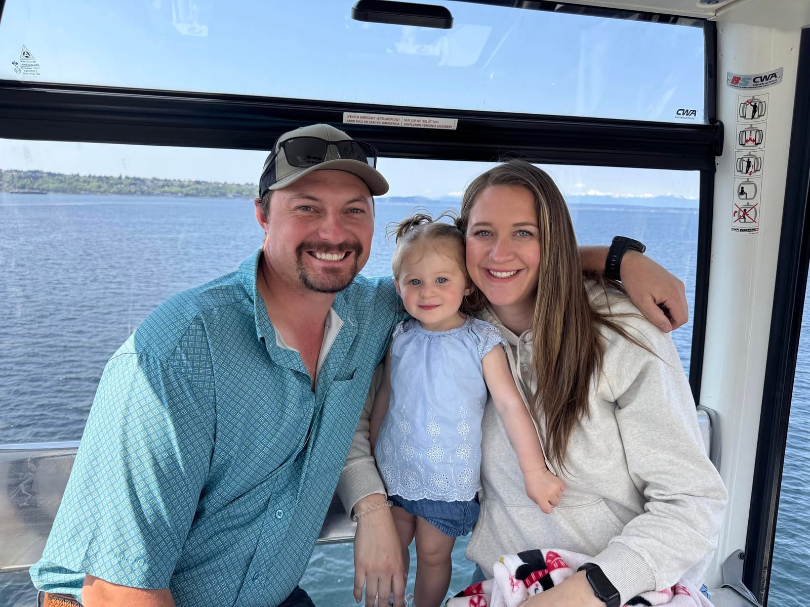 Mitch, Kaitlyn, and their daughter smiling together on a boat on a lake.